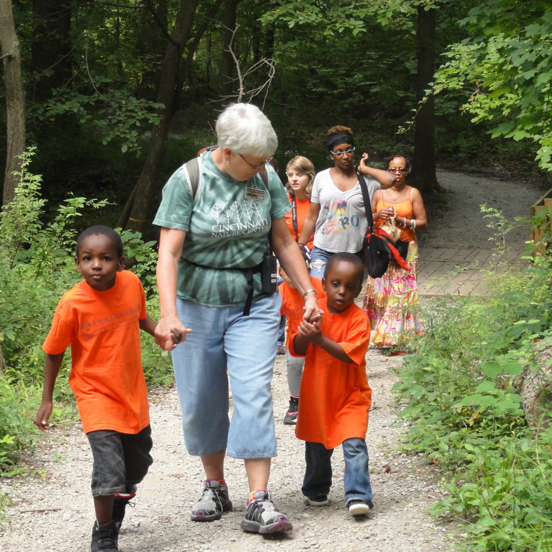 A volunteer walks with young children down a trail